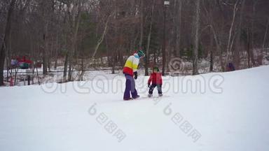 年轻人<strong>滑雪板</strong>教练教小男孩如何骑<strong>滑雪板</strong>。 冬季活动概念。 慢镜头
